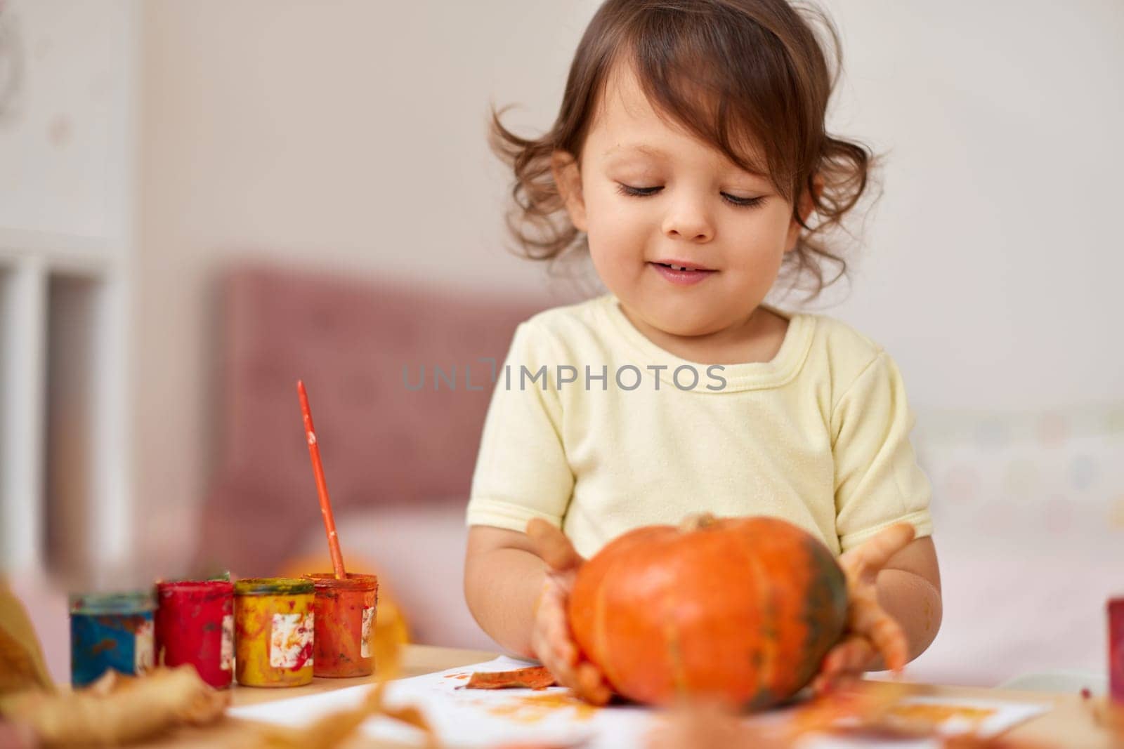 happy little child girl painting Halloween pumpkin. smiling baby girl drawing autumn pumpkin in yellow paint
