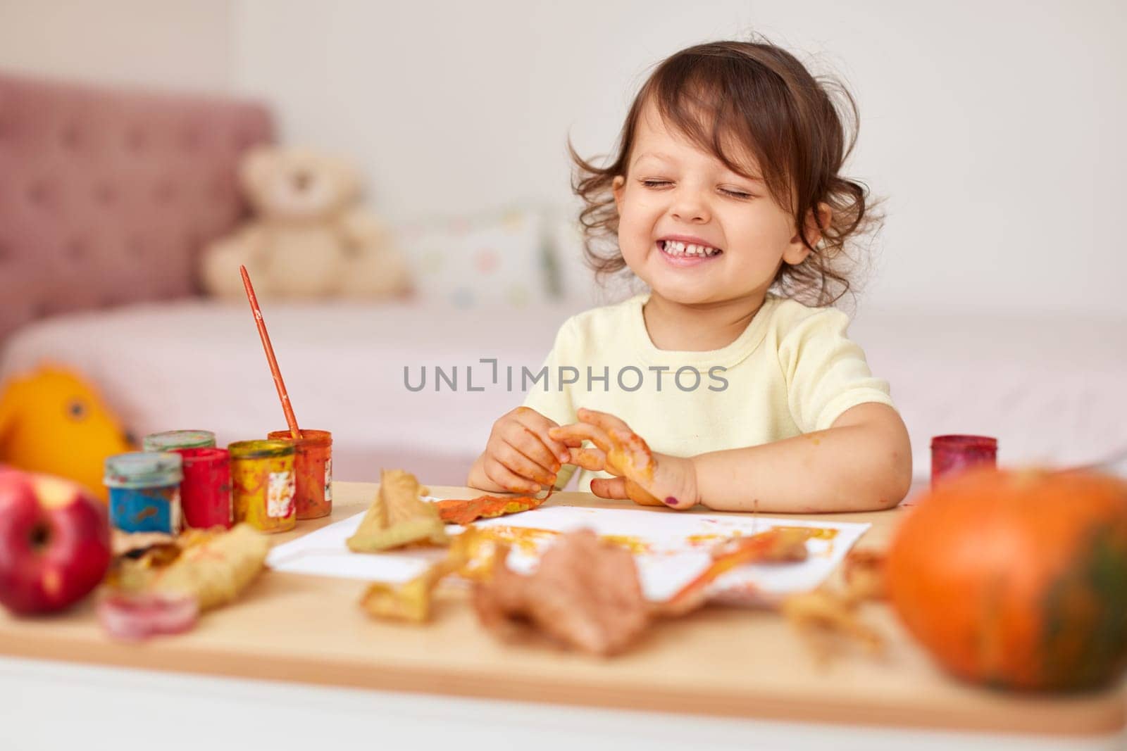 happy little baby girl painting autumn leaves. baby girl drawing leaves in yellow and orange paint