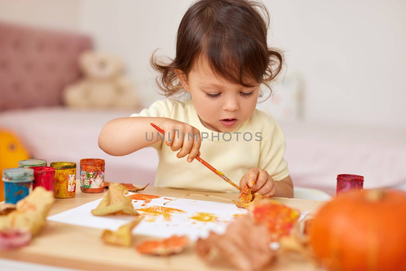 cute little child girl painting autumn leaves. baby girl drawing leaves in yellow and orange paint