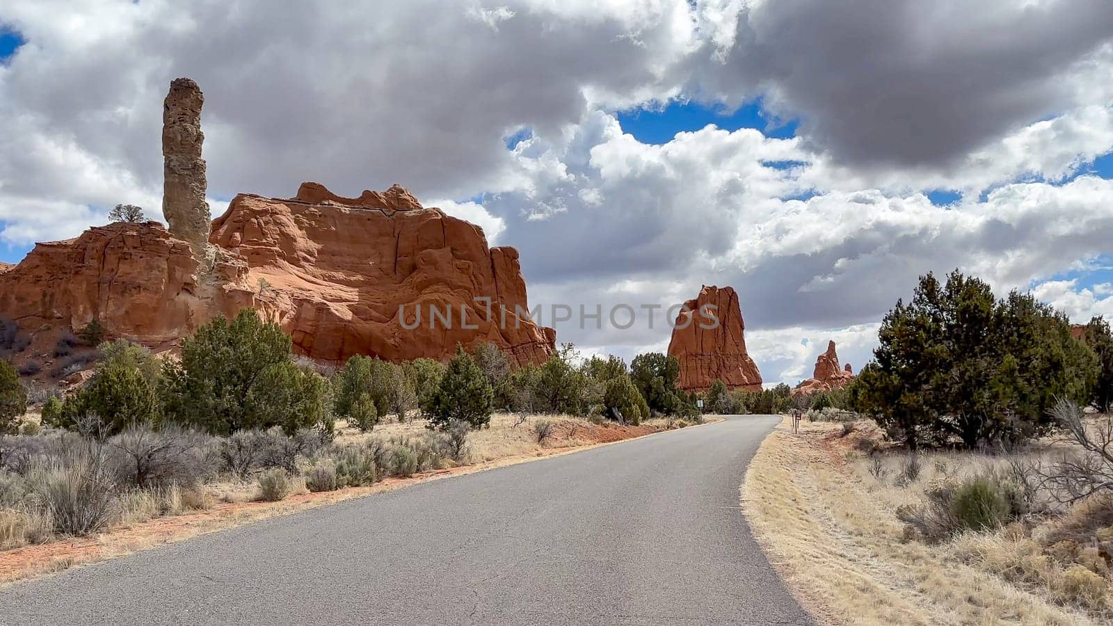 View of the Scenic Park Road in Kodachrome Basin State Park in Utah, USA. The red rock formations and spires are stunning against the bright blue sky and white clouds.