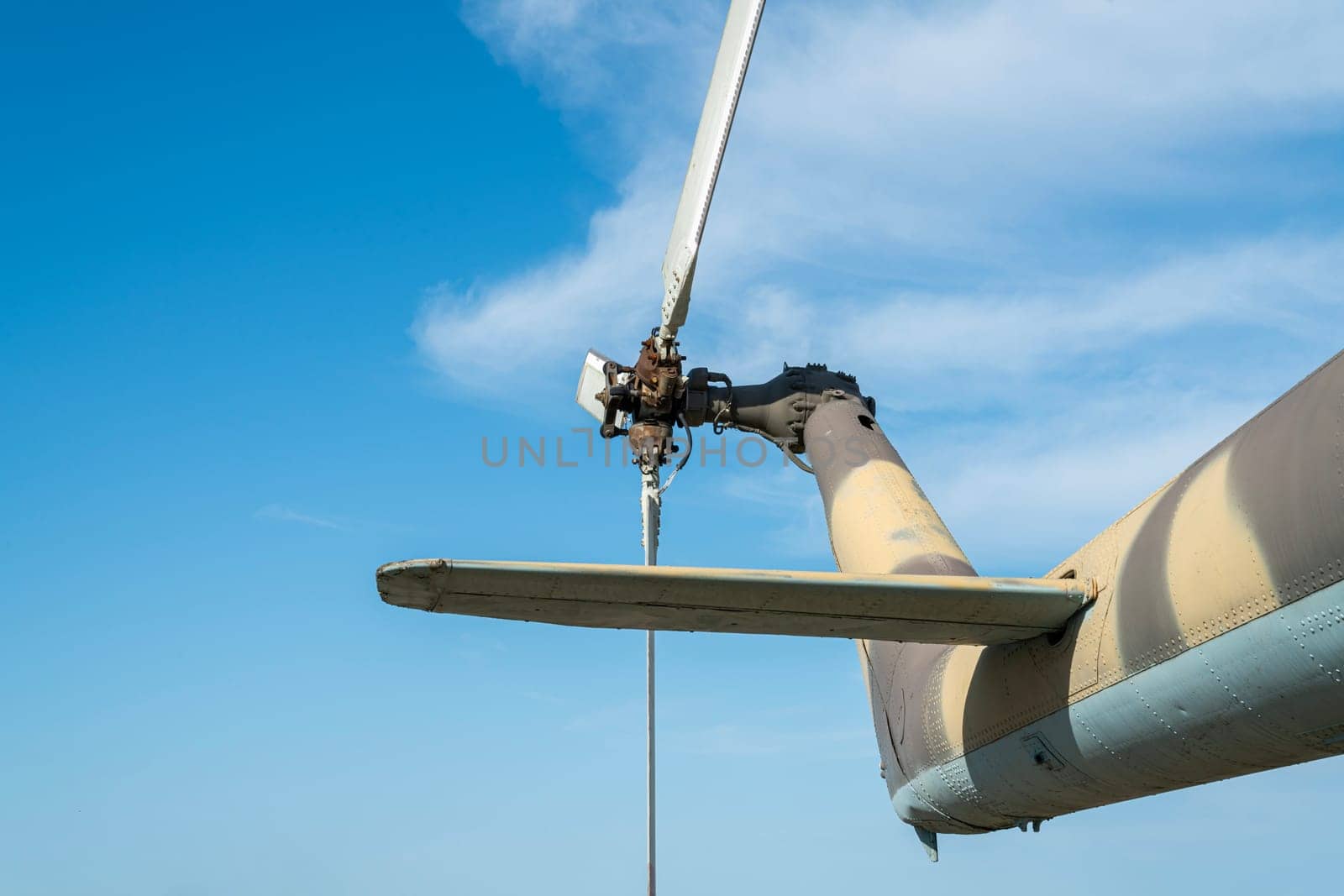 The view features the rotor blades of a helicopter, highlighting their intricate design against a vibrant blue sky. The helicopter's body showcases a camouflage pattern.