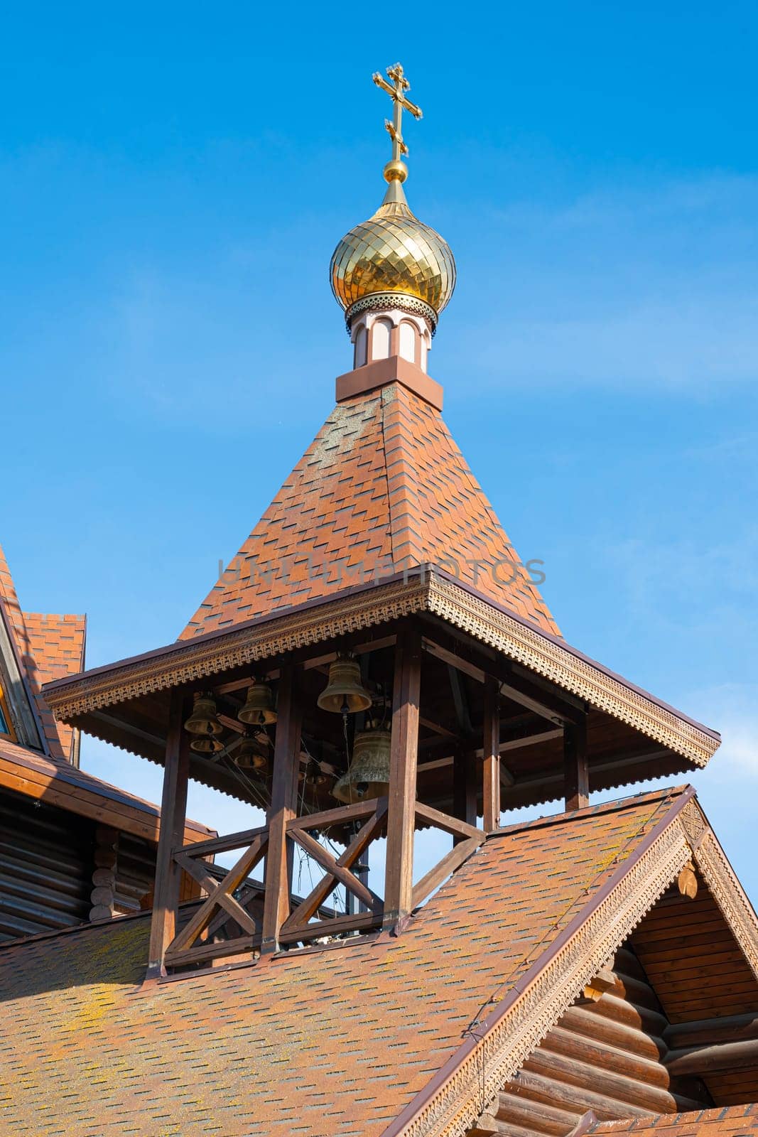 A striking wooden church structure features a golden dome and a bell tower, with bright blue skies in the background. The architectural design reflects traditional elements.
