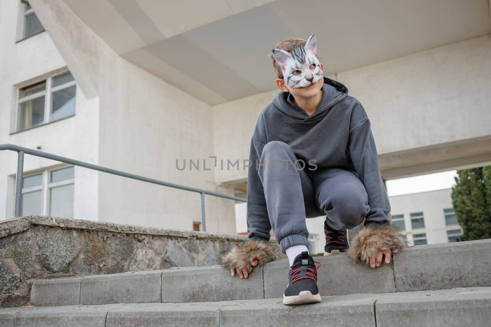 Teenager wearing cat mask and gloves performs quadrobics in the city, imitating the movements of a cat