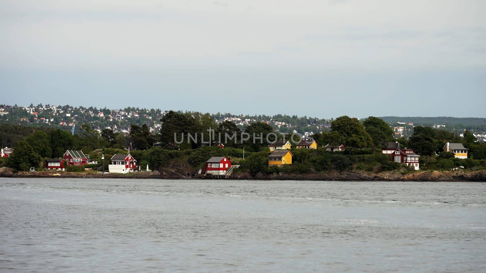 Natural landscape with rippling river and houses by the coast. Action. Countryside region, view from the river on a small town and green trees
