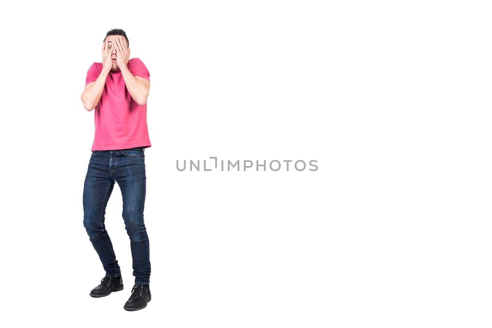 Full length scared man in casual clothes covering face with hands and peeking through fingers isolated on white background