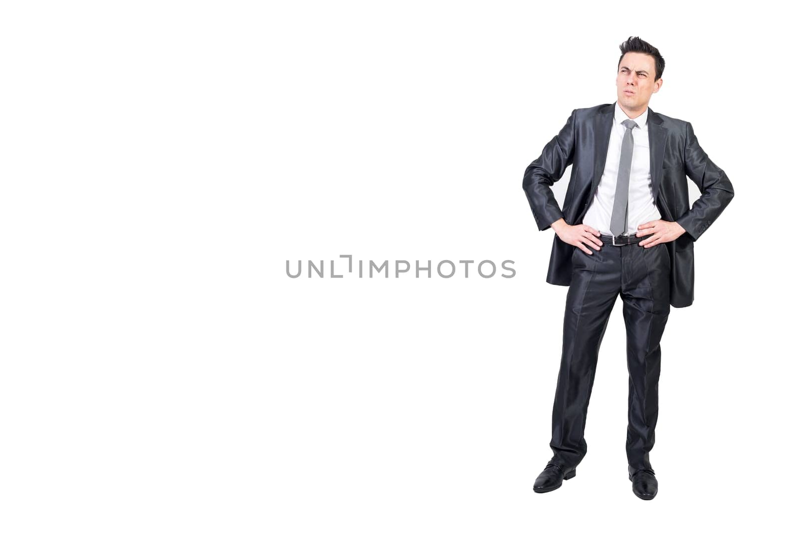 Full body of comic male entrepreneur in suit expressing doubt and looking up while standing with hands on waist against white background