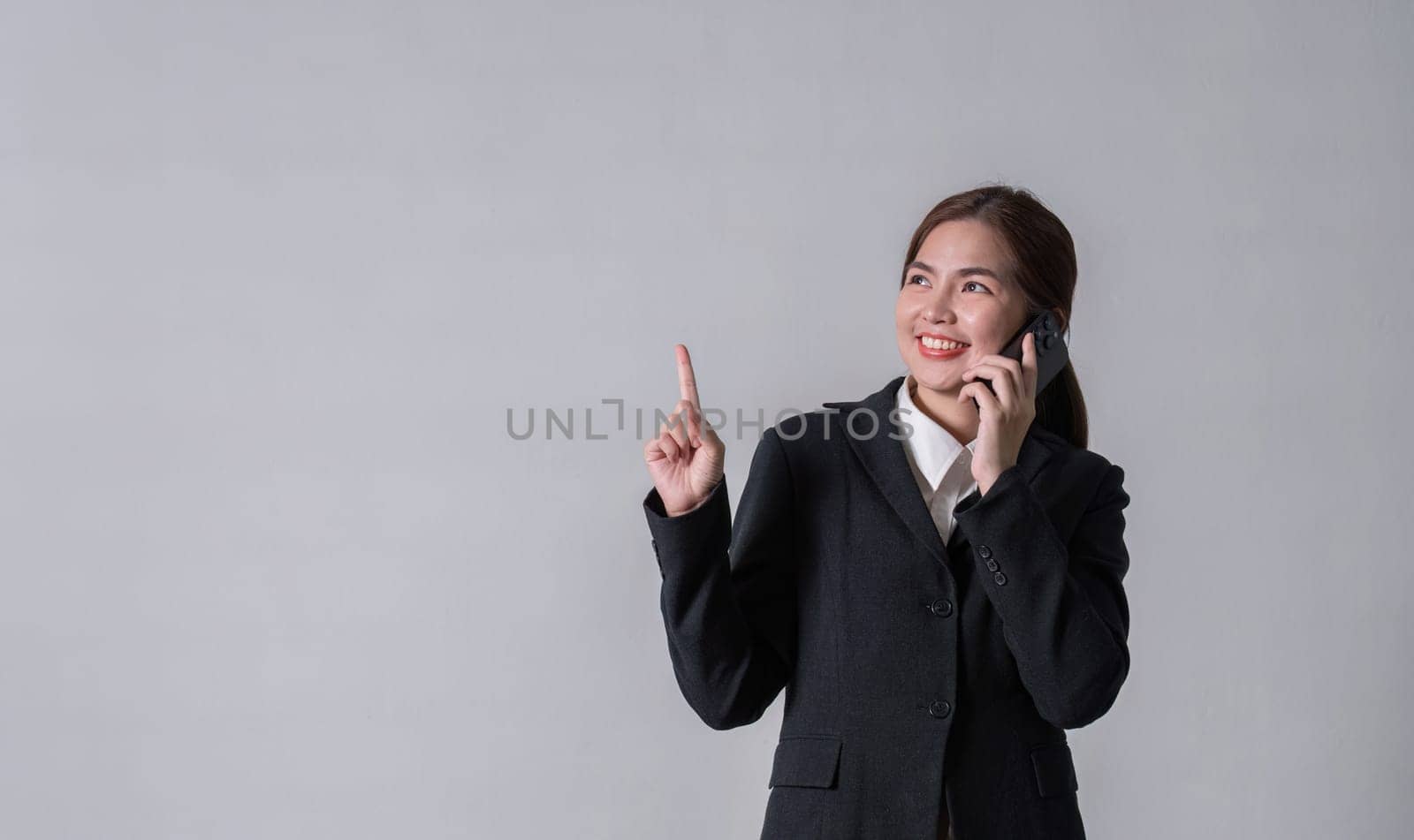 Portrait of a young business woman standing and talking on the phone, pointing, focus according to thoughts..