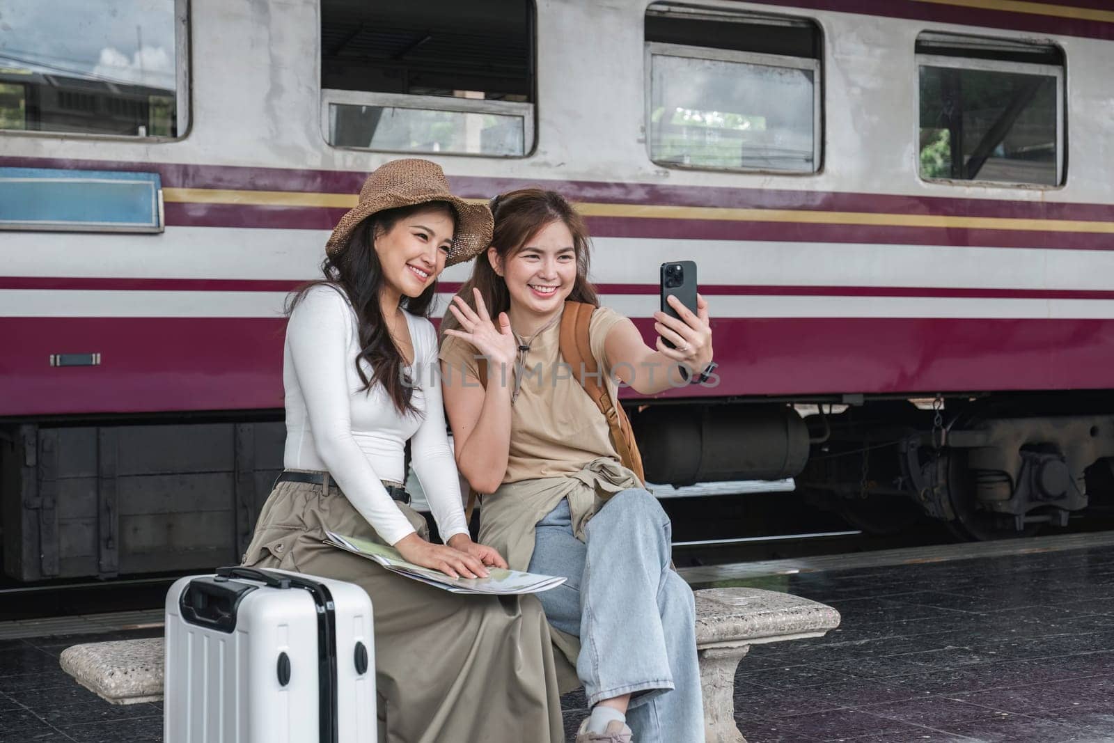 Two young female tourists are happy while waiting for their train at the train station to leave for their holiday. by wichayada