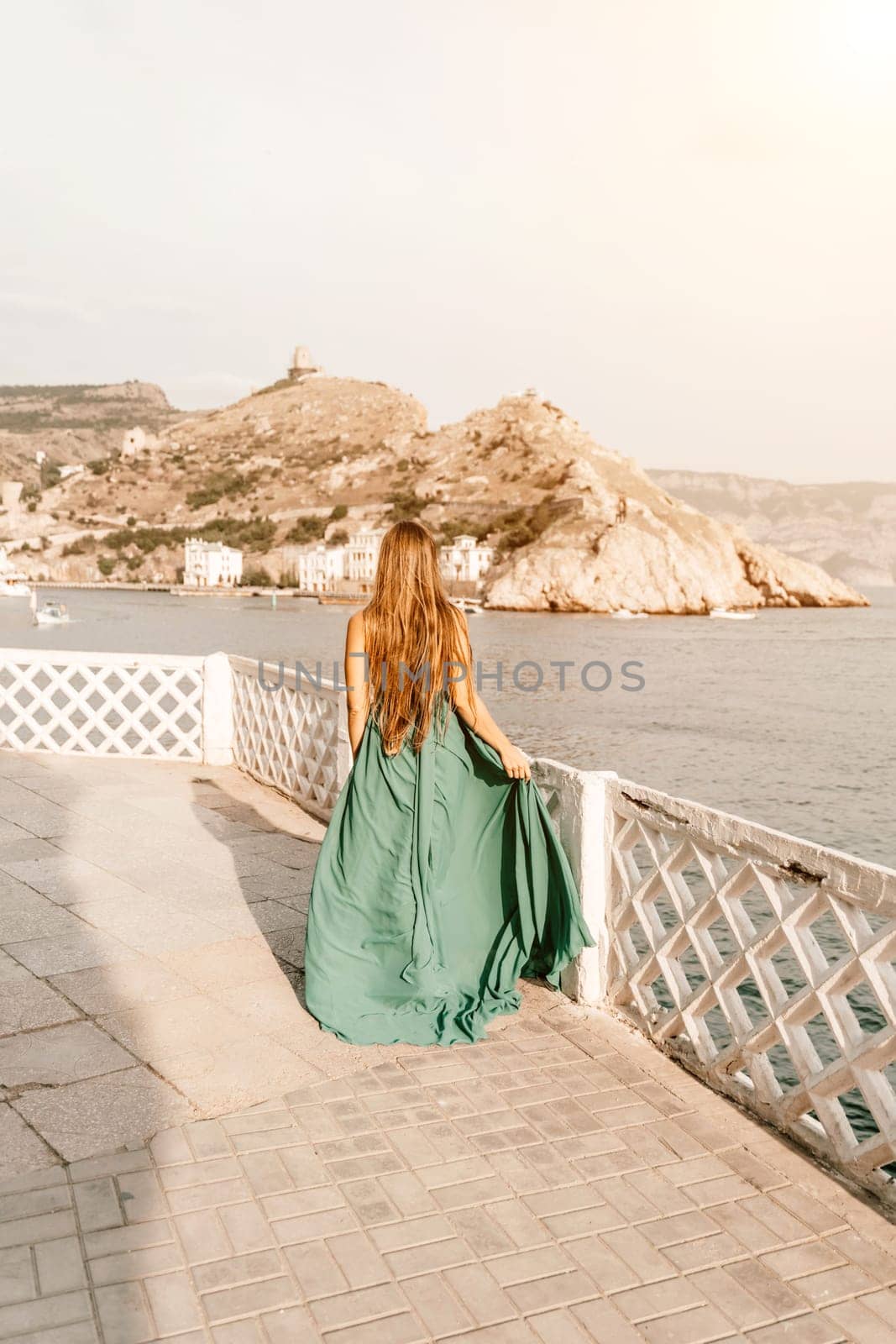 Woman sea trevel green dress. Side view a happy woman with long hair in a long mint dress posing on a beach with calm sea bokeh lights on sunny day. Girl on the nature on blue sky background. by Matiunina