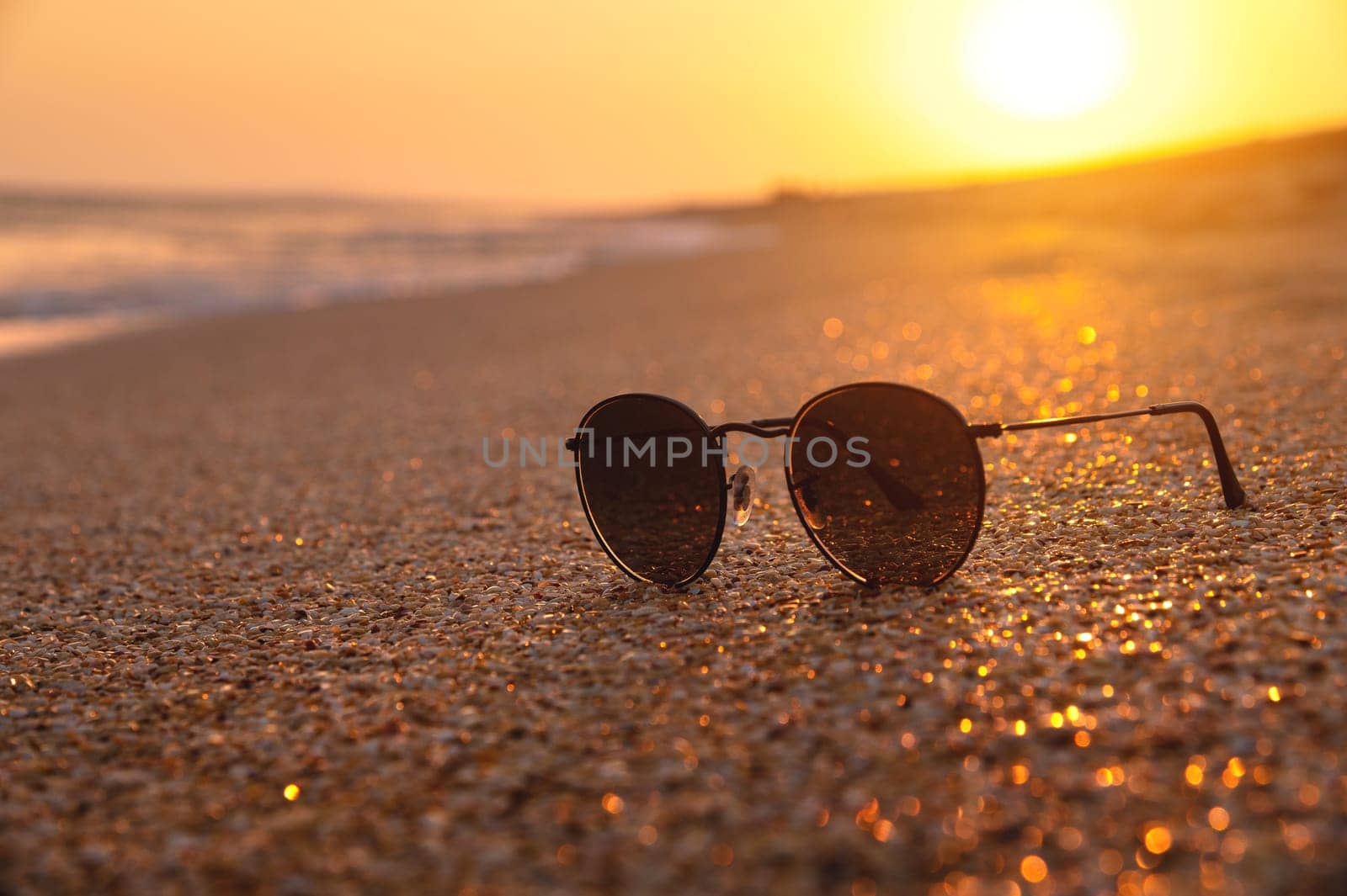 Sunglasses on the beach, lie on the sandy sand at sunset. Concept of beach holiday, serenity.