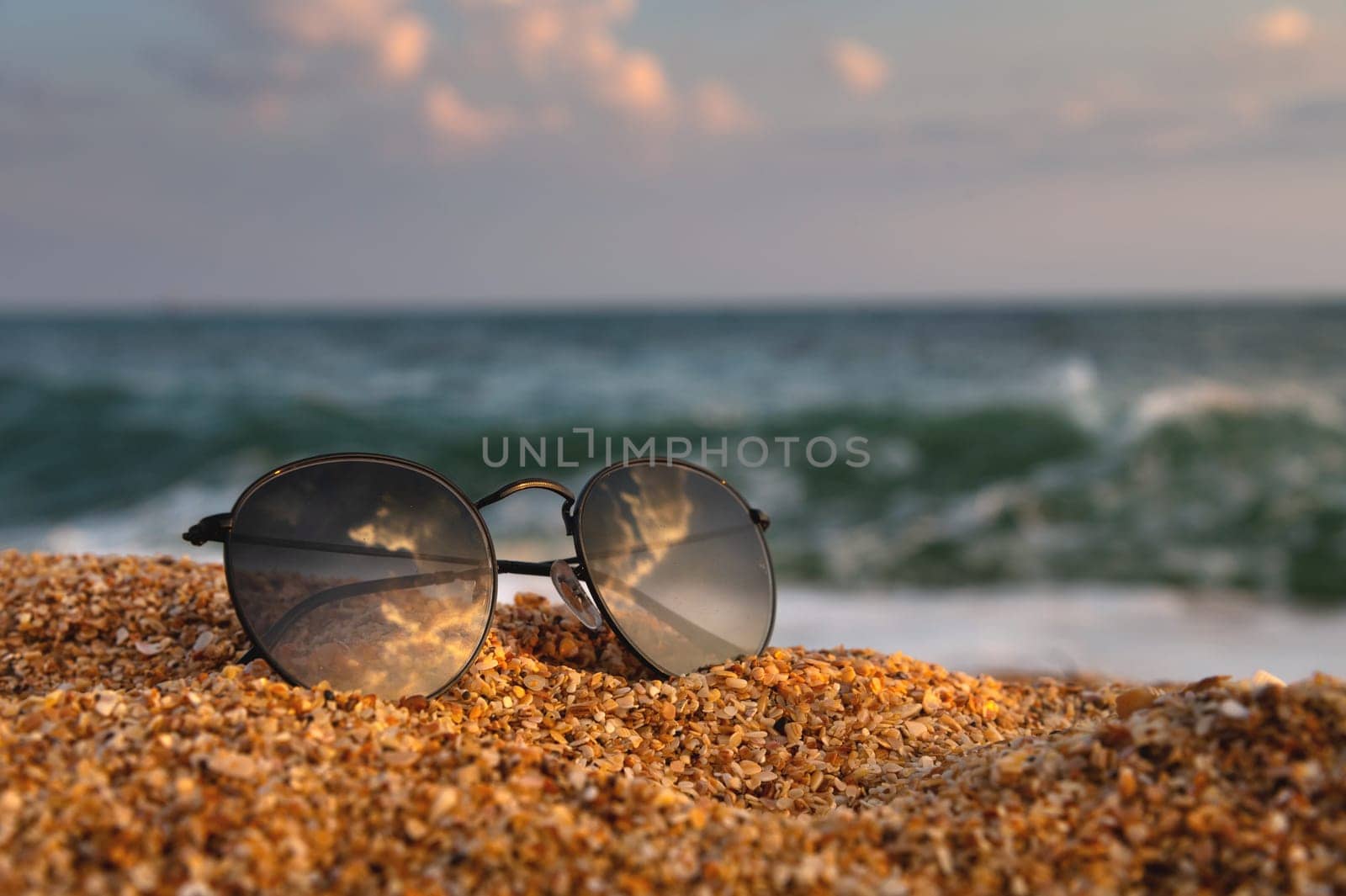 On the beach, sunglasses lie on the sand in the background a wave rolls from the sea. Close-up of leisure accessory, no people by yanik88