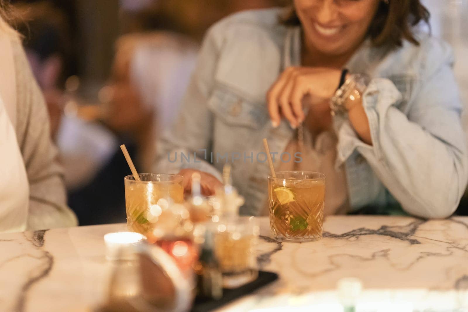 Smiling women drinking alcoholic cocktails at the bar at the table. Mid shot
