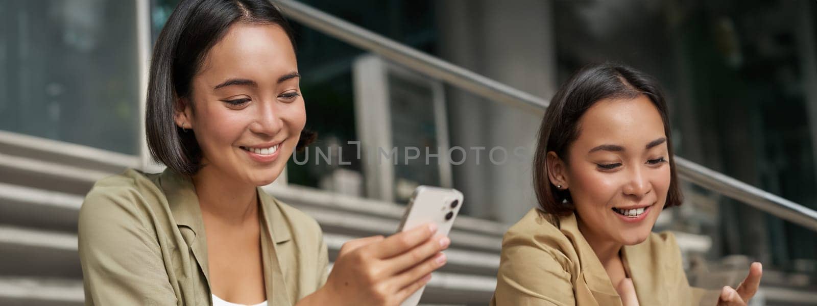 Portrait of asian girl takes selfie on mobile phone. Korean woman smiling, video chat on smartphone app while sits outside on stairs by Benzoix