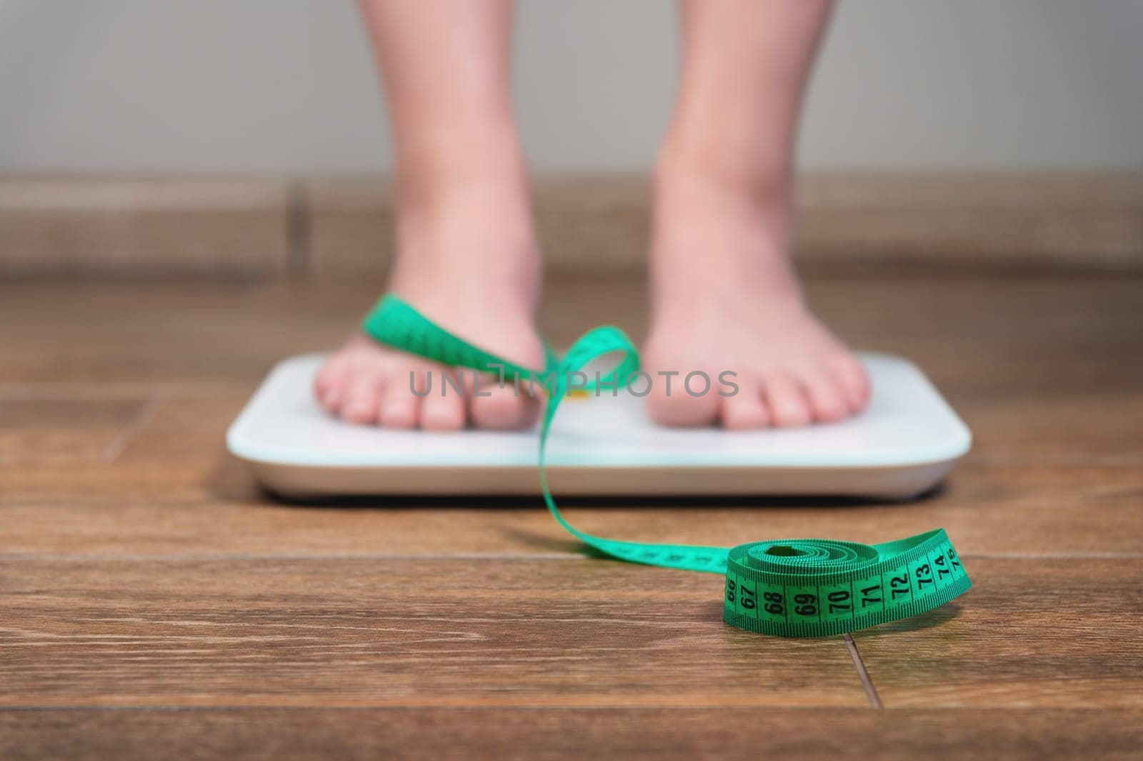 Unrecognizable woman standing on the scales, checking her weight, focused on the measuring tape. Cropped view of caucasian girl struggling with extra pounds using weight loss diet.