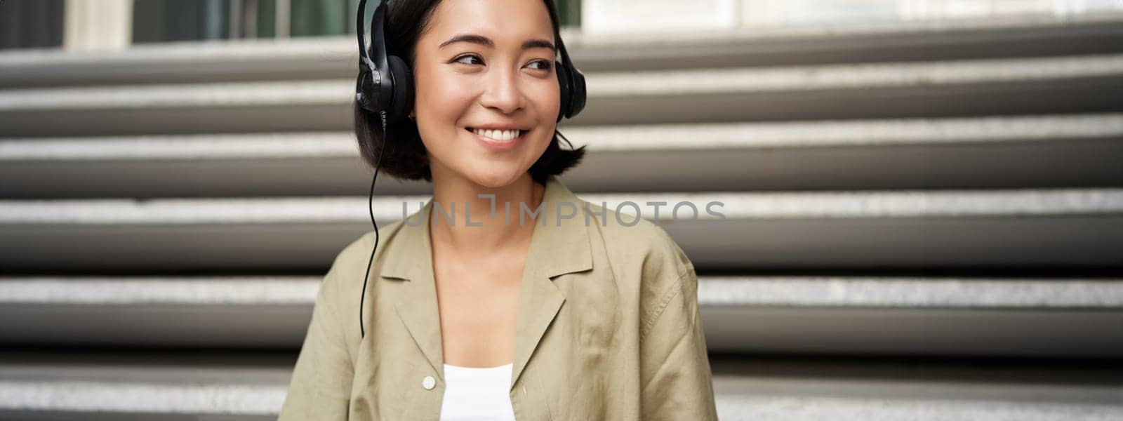 Portrait of beautiful girl in earphones, listening music, smiling and walking in city centre.