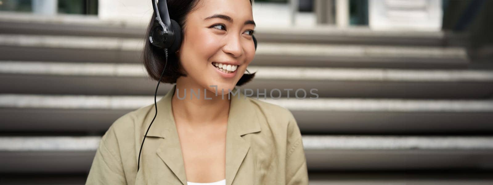 Portrait of beautiful girl in earphones, listening music, smiling and walking in city centre.