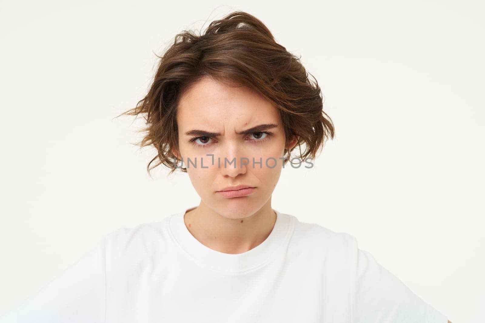 Close up of brunette woman shows angry face, frowning grumpy, pouting and looking disappointed, standing over white background. Copy space