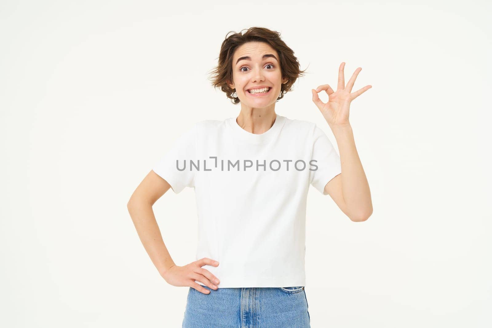 Portrait of woman smiling, showing okay sign with confidence, gives approval, recommends smth good, stands over white background.