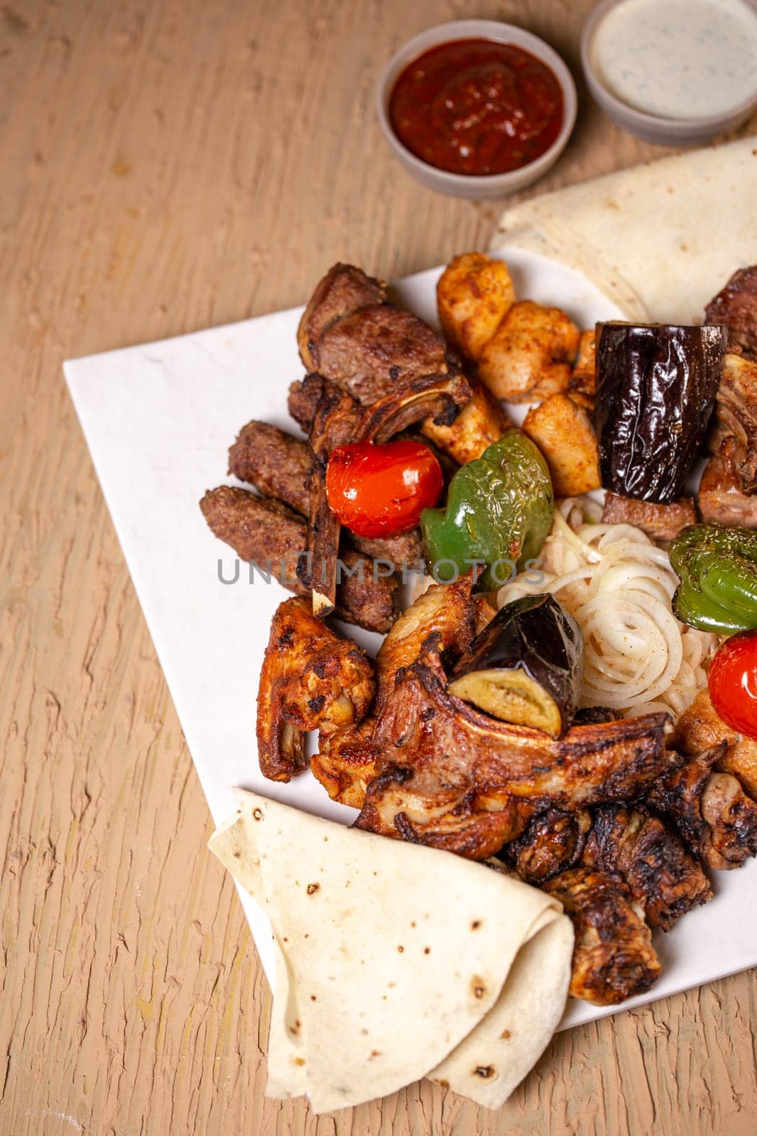 top view of a delicious fresh kebab made of different meats with sauce and vegetables.