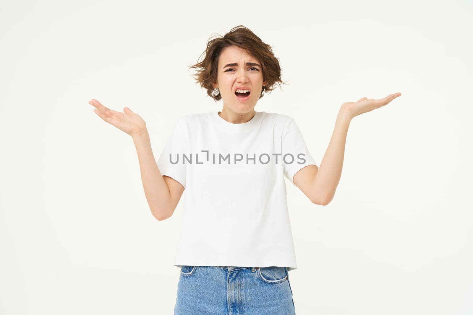 Portrait of confused woman, shrugging shoulders and looking upset, cant understand something, frustrated, standing over white studio background.