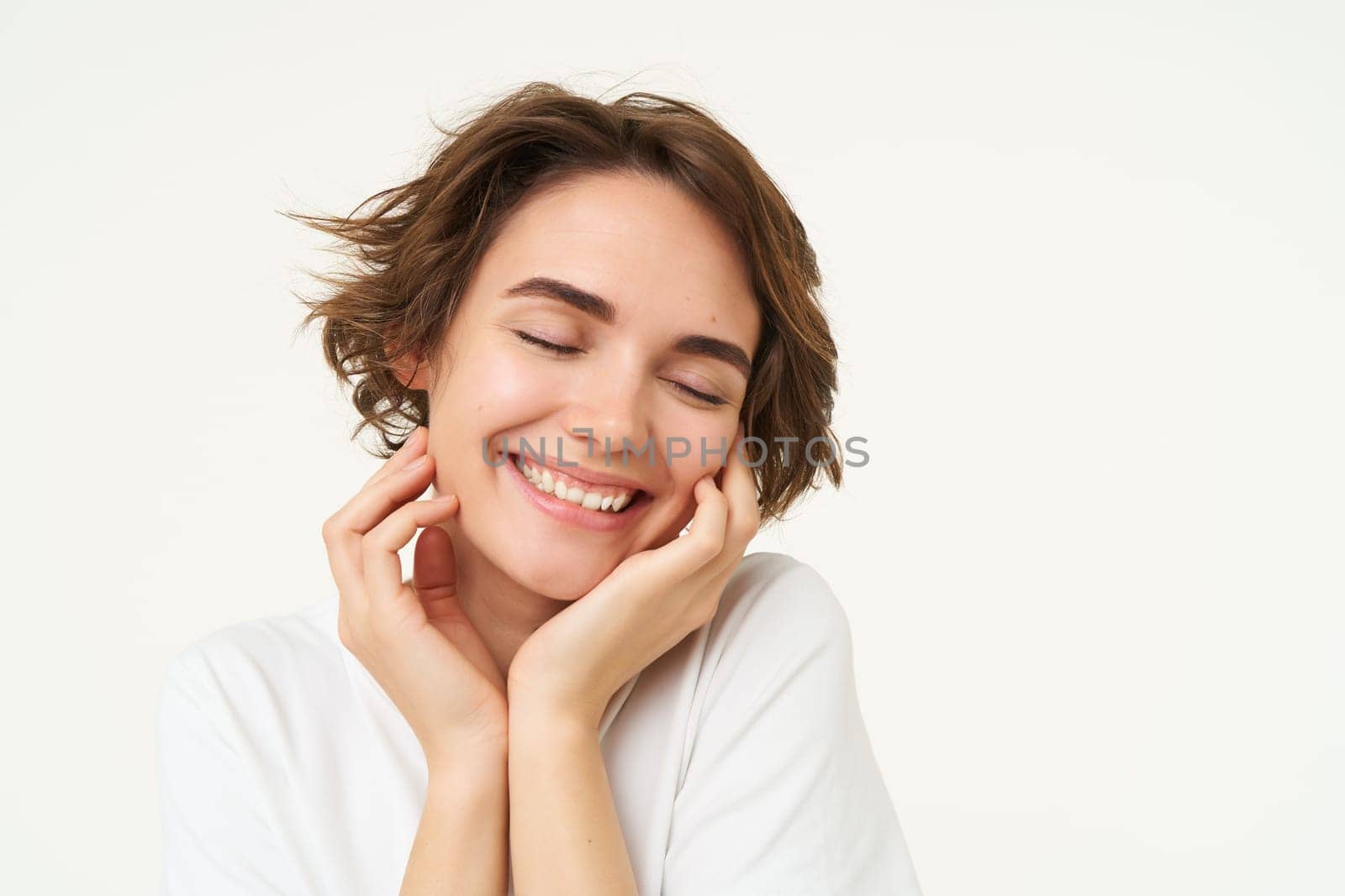 People and emotions concept. Young woman touches her face, smiling, pleased with her face condition after skincare treatment, stands over white background.