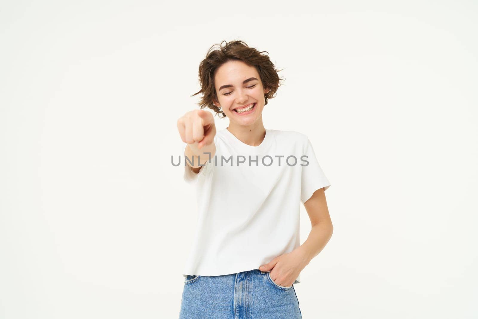 Portrait of excited, smiling young woman, pointing finger at camera, inviting you, congratulating, standing over white studio background by Benzoix