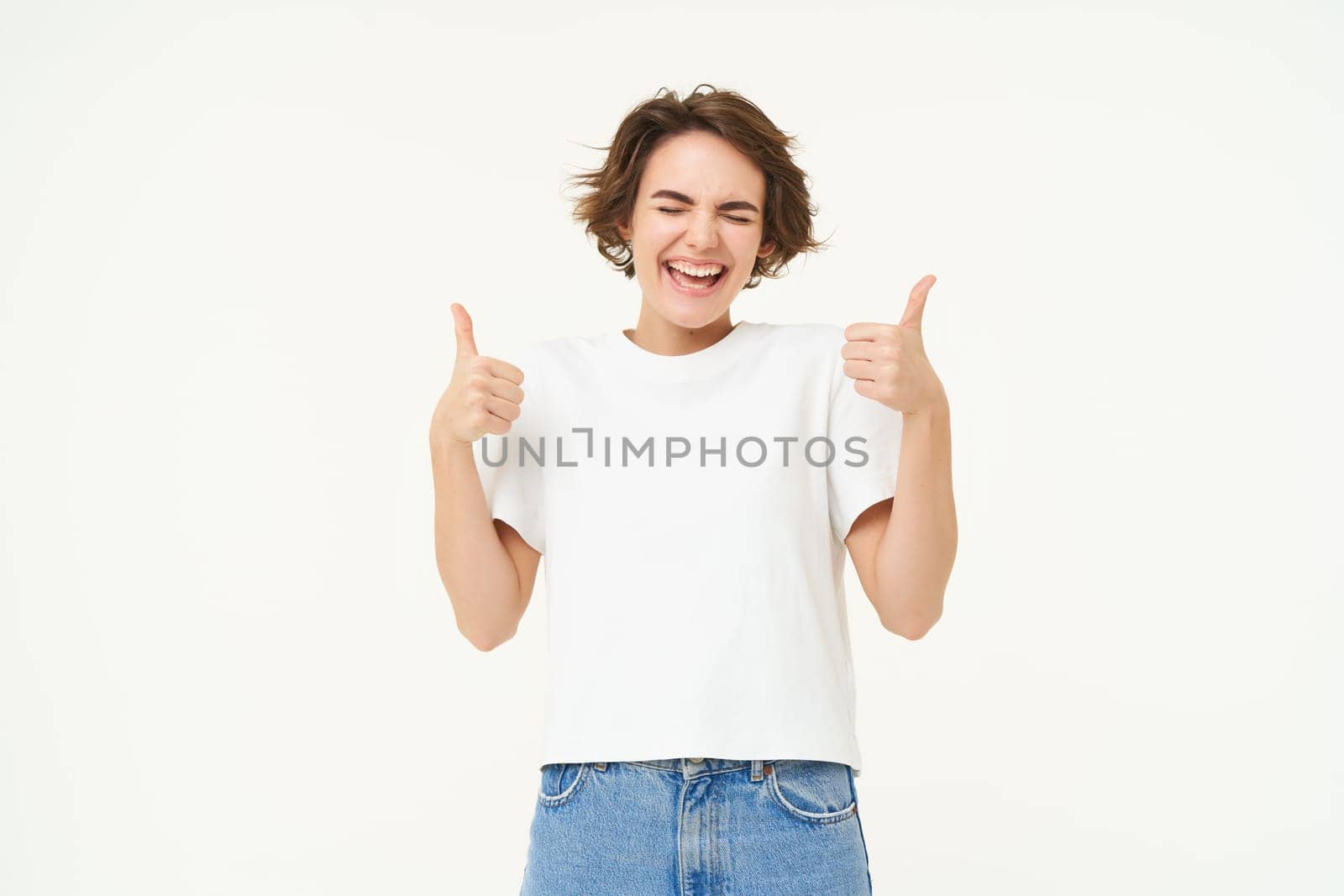 Portrait of cheerful young woman, shows thumbs up in approval, like something good, nod in approval, looking confident, standing over white background by Benzoix