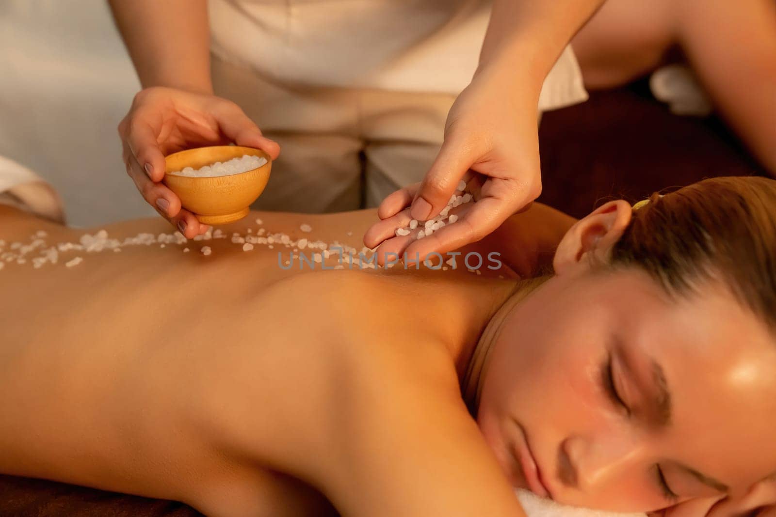 Closeup couple customer having exfoliation treatment in luxury spa salon with warmth candle light ambient. Salt scrub beauty treatment in Health spa body scrub. Quiescent