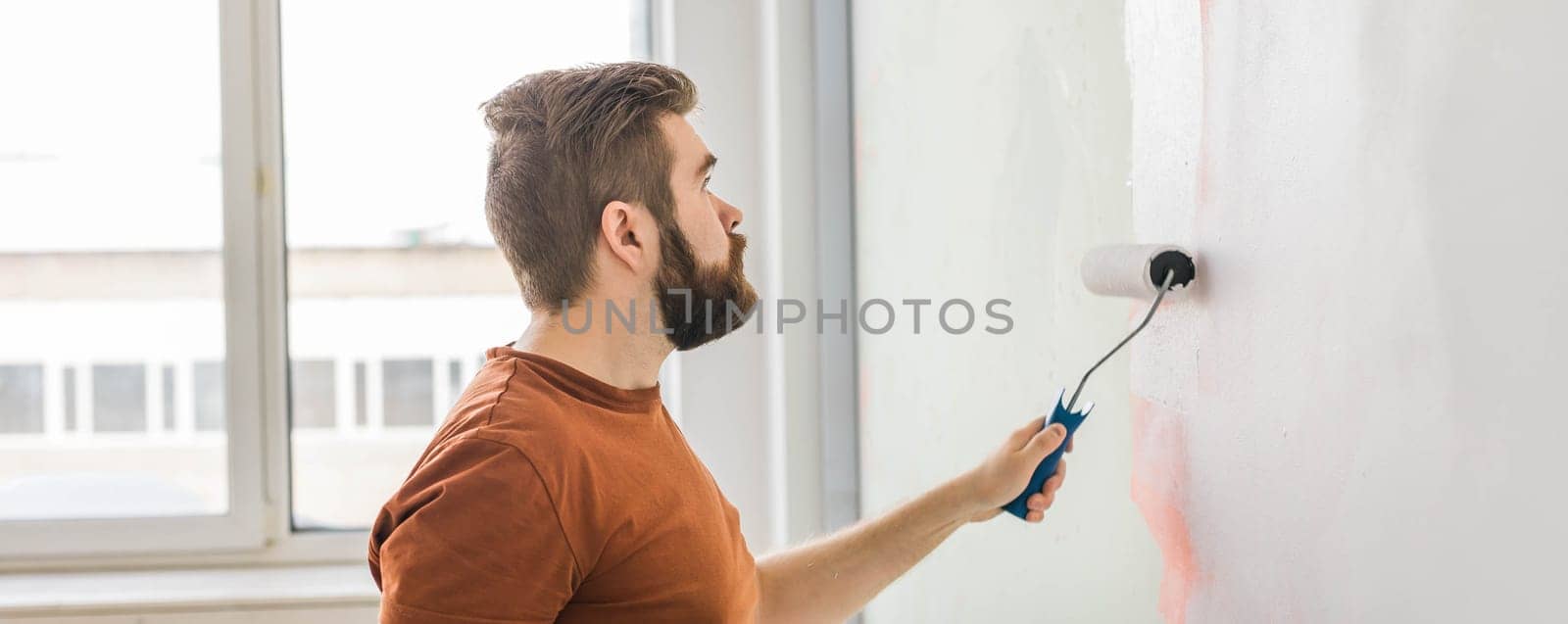 Man painting wall with paint roller - renovation and redecoration