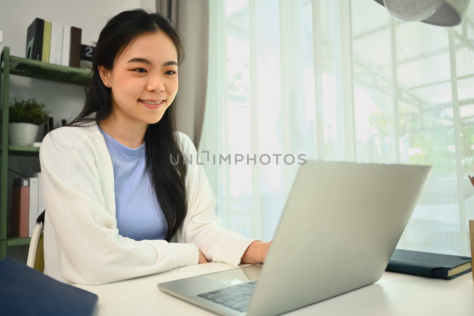 Satisfied Asian female freelancer searching information, working on laptop computer at home.