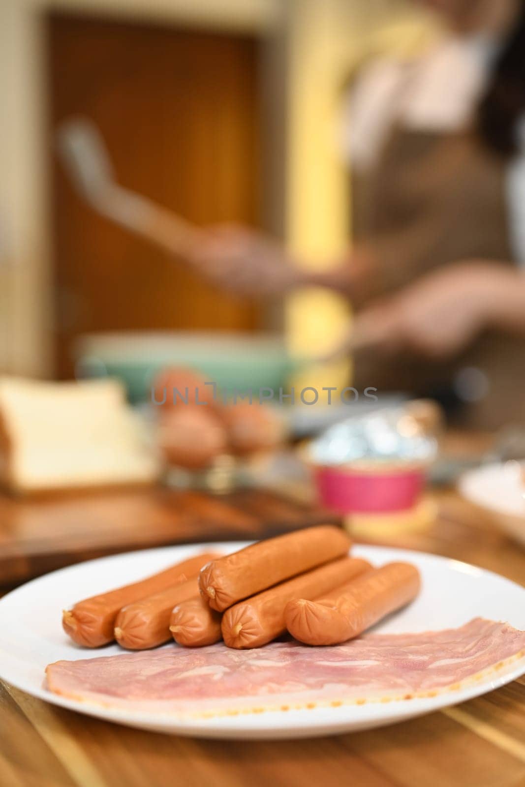 Close up a white plate of sausages and bacon on a wooden kitchen counter for breakfast.