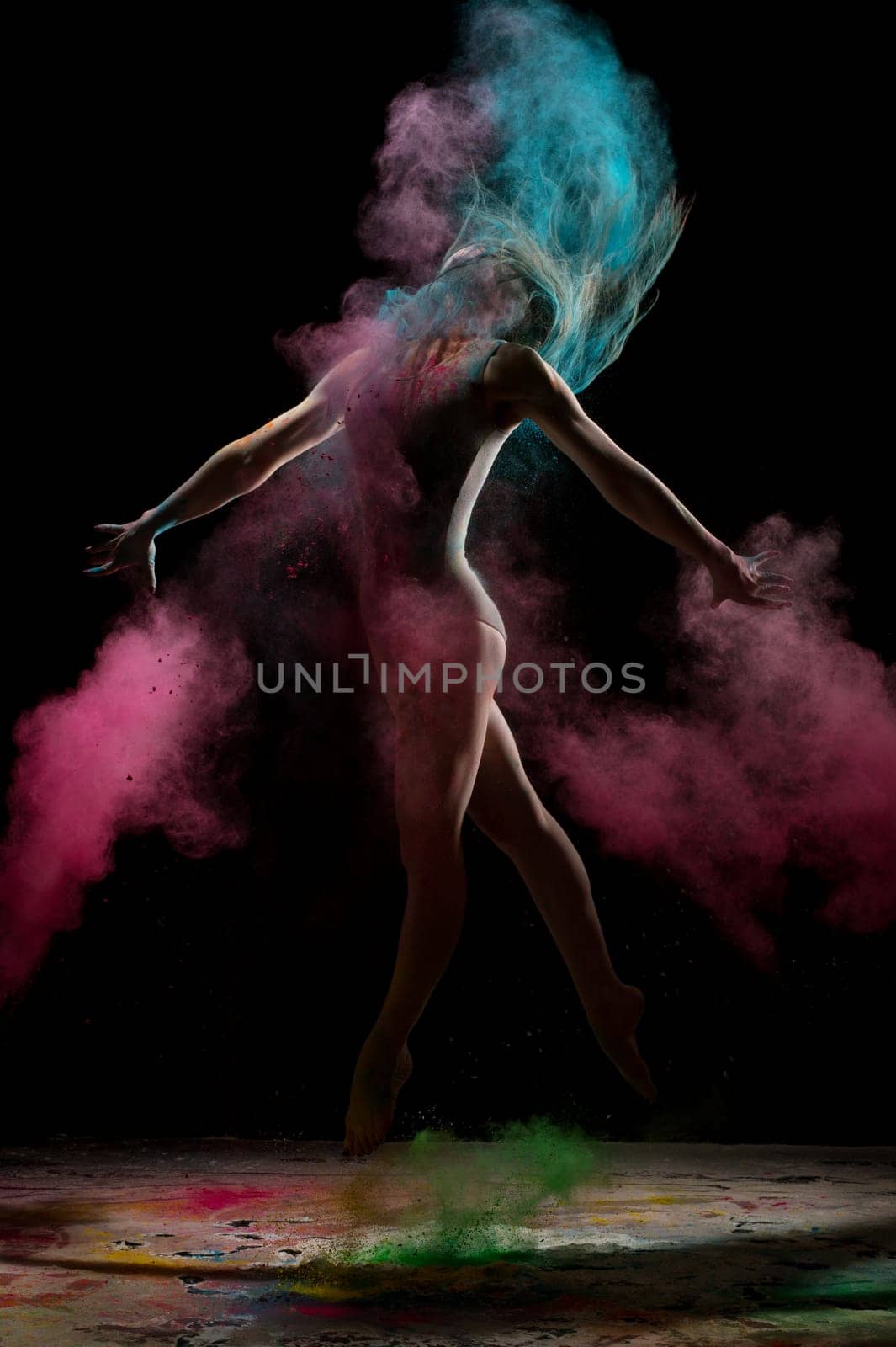 Slim blonde in gray body jumping in color dust cloud in the dark room