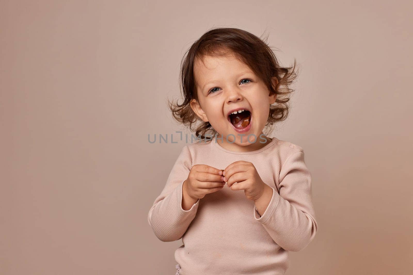 smiling child girl holding fruit pastille on beige background. healthy baby food.