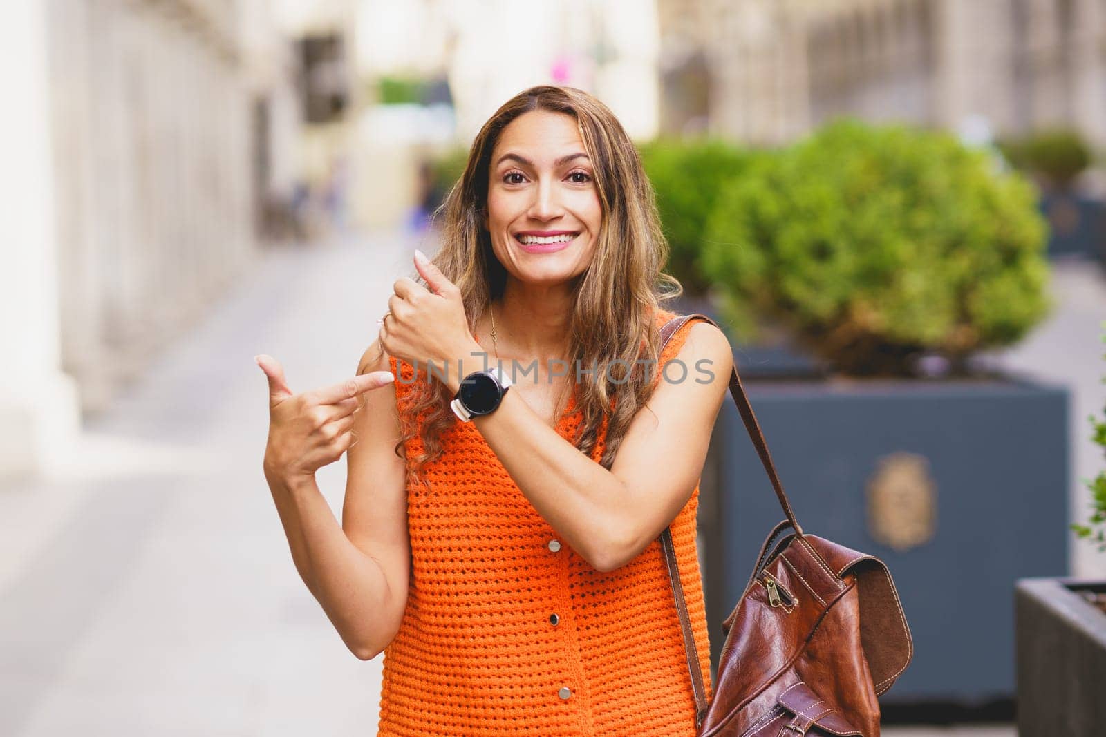 Latin smiling woman pointing to her smart wrist watch in the street