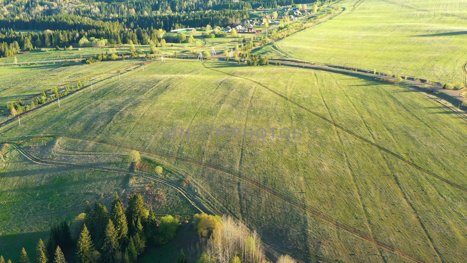 Top view of beautiful green fields and forests on sunny day. Clip. Green fields with roads and village in forest parts. Landscape of village road and houses with green fields and forests in summer.