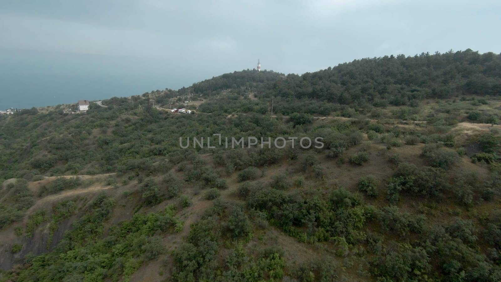 Top view of mountains with sea horizon and lighthouse. Shot. Beautiful landscape with mountains on coast and sea in distance.