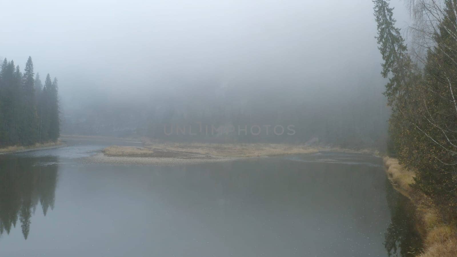 Top view of misty lake with green forest. Clip. Beautiful and mysterious lake with fog on cloudy day. Romantic frightening lake with dense fog and forest.
