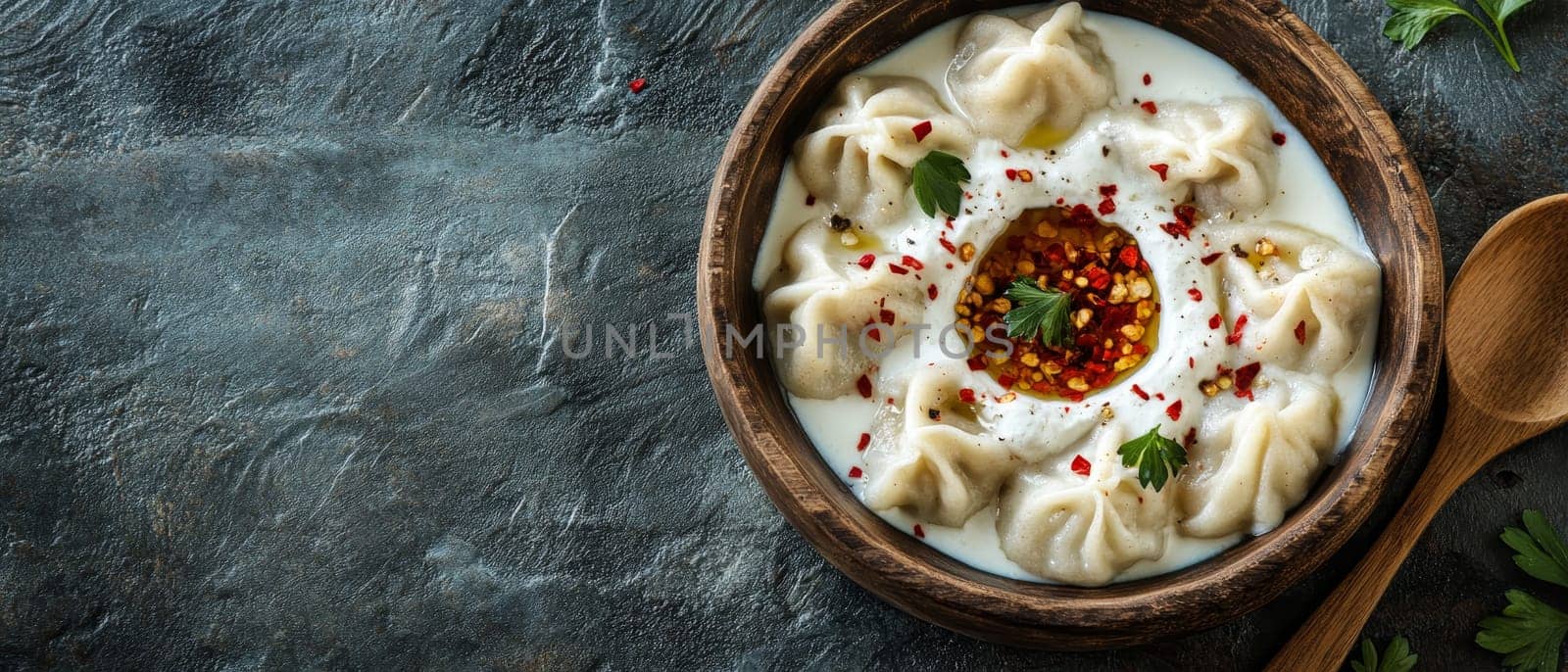 Traditional Georgian khinkali dumplings served in a creamy yogurt sauce with red chili oil and herbs in a rustic wooden bowl.