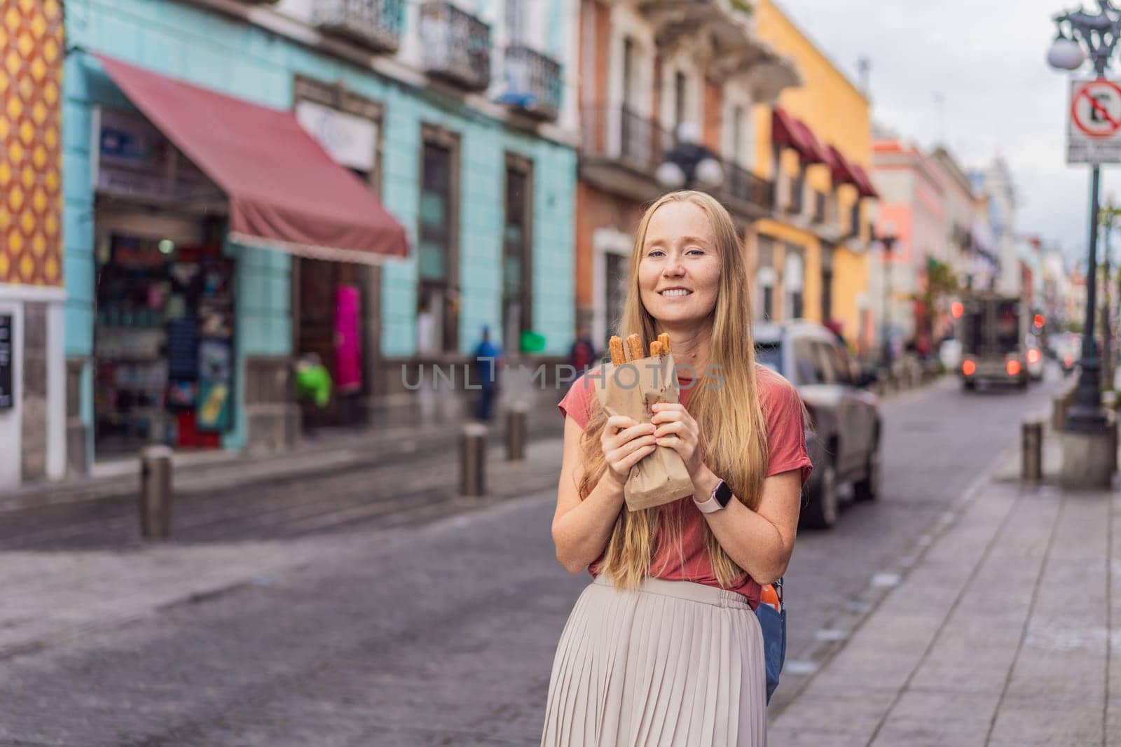 Female tourist eating churros on a colonial street in Puebla, Mexico. Cultural experience, local cuisine, and street food exploration concept.
