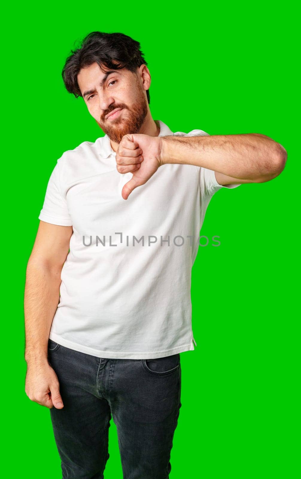 A man expresses disappointment with a thumbs down gesture against a bright green background close up