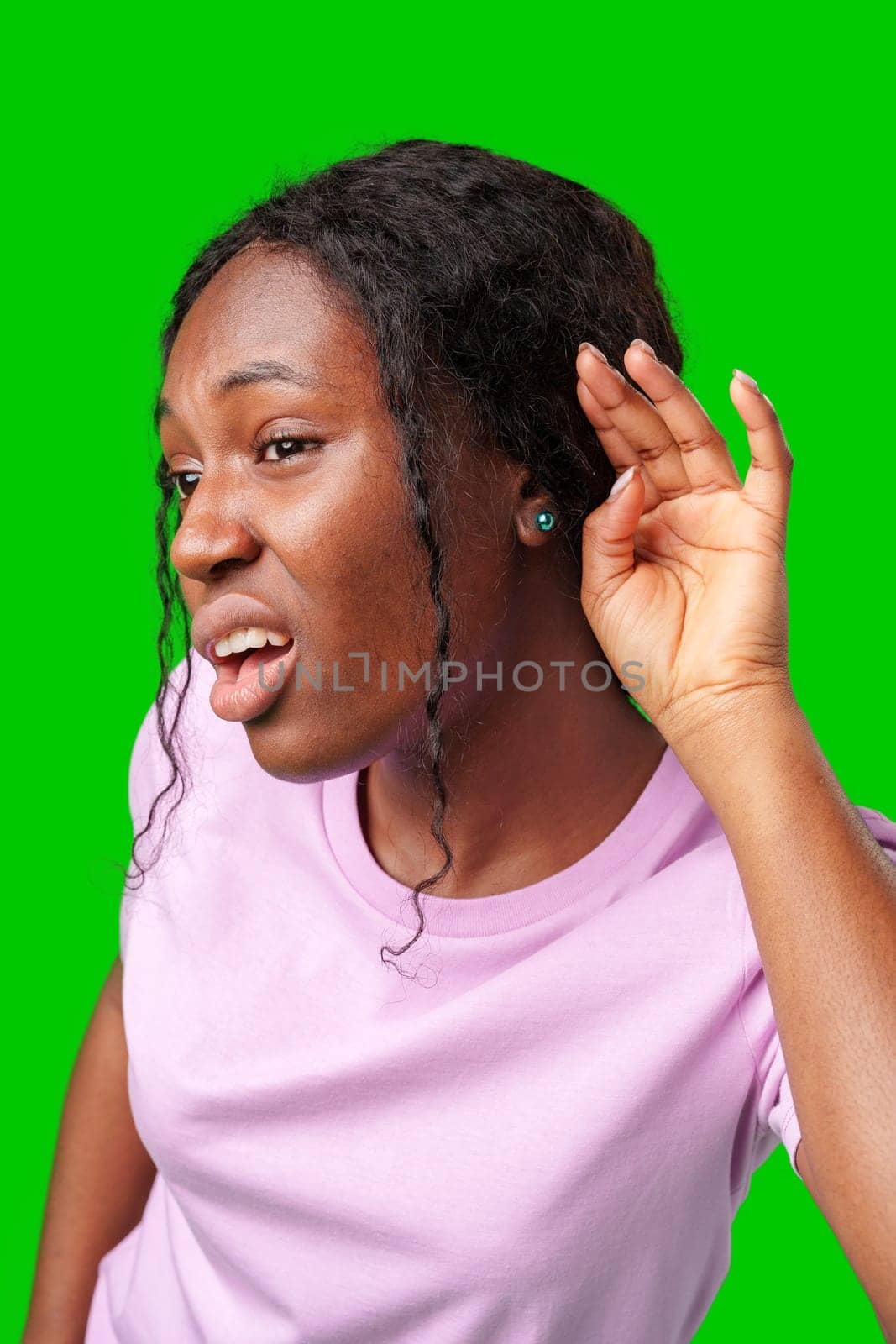 Young woman playfully listening with a smile against a vibrant green background in studio