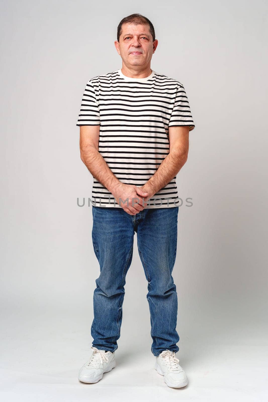 A man stands confidently in a striped shirt, casual jeans with a neutral background in studio
