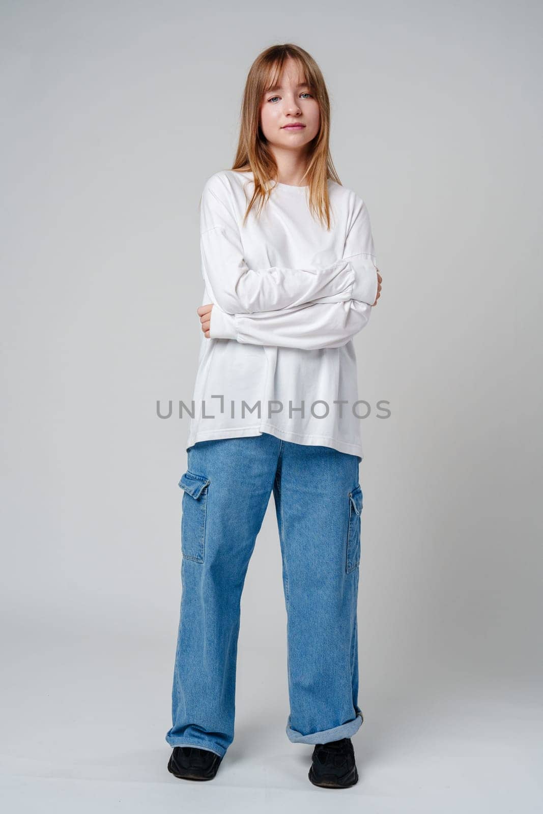 Young woman with long hair in a white sweatshirt standing against a light gray background close up