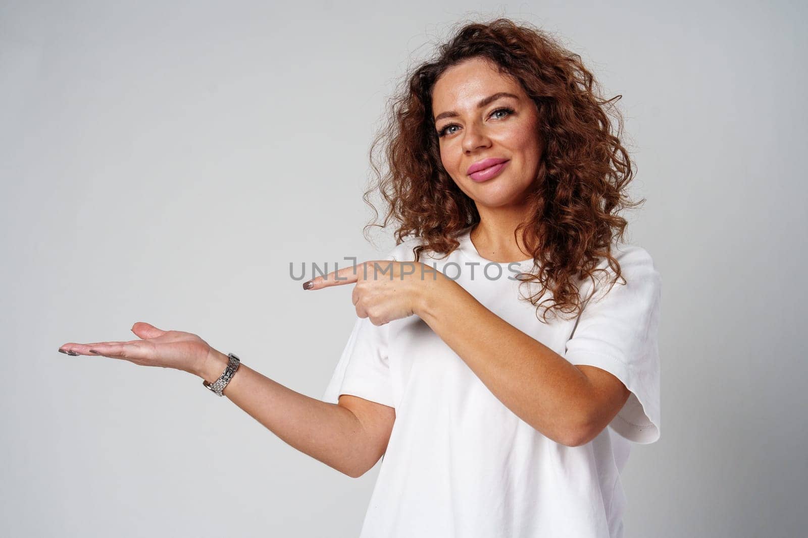 A young woman with curly hair playfully pointing finger while standing against a gray background in a casual setting