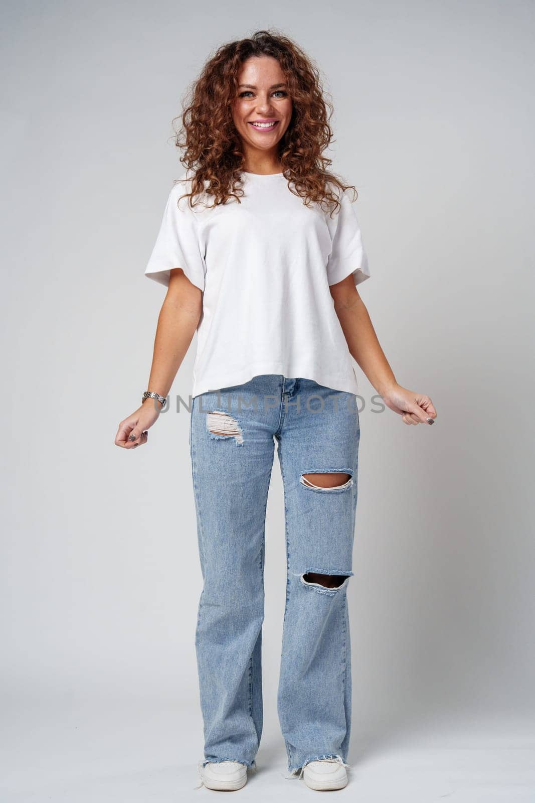 A woman in a white shirt and ripped jeans posing positively with a playful expression in a light studio setting close up