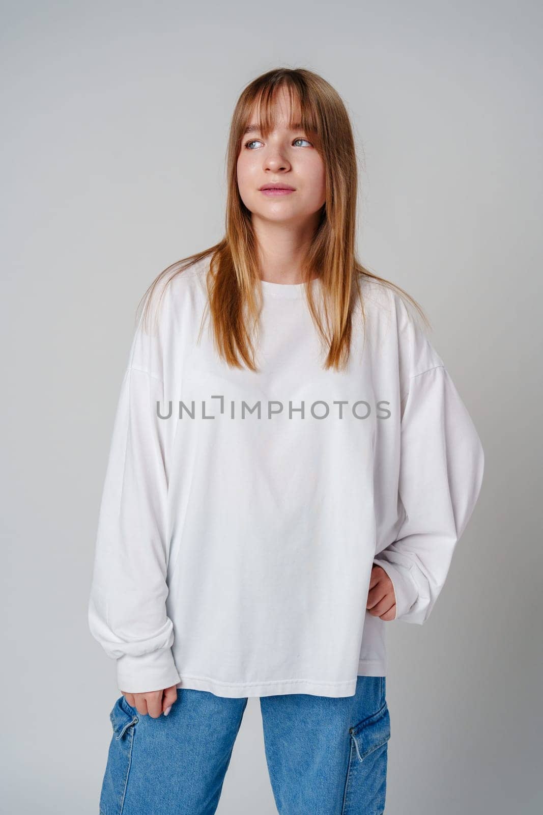 Casual portrait of a young girl wearing a white long-sleeve shirt and blue jeans in a minimalist studio close up