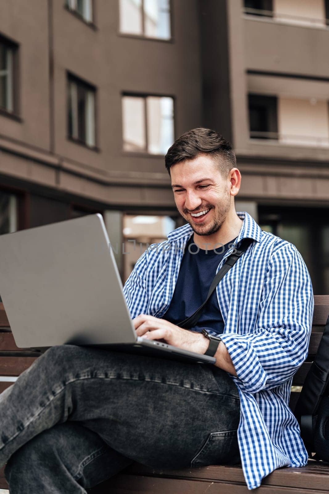 Young man working on a laptop while seated on a bench outside close up