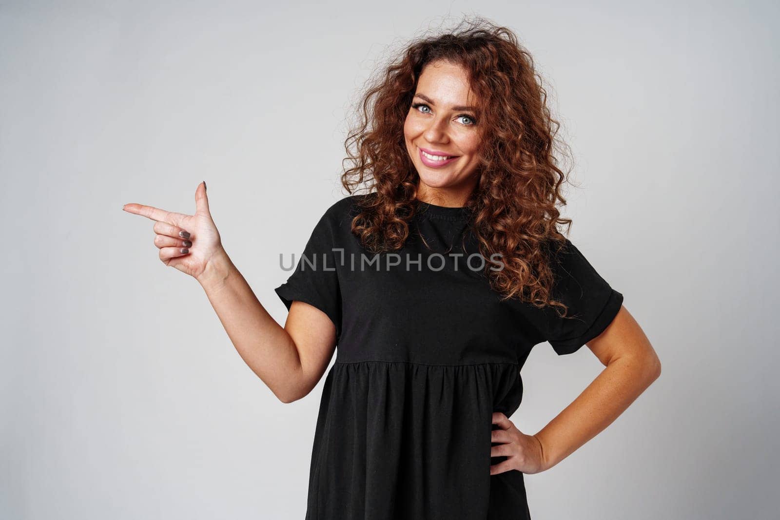 Cheerful woman with curly hair gestures playfully against a light gray background close up