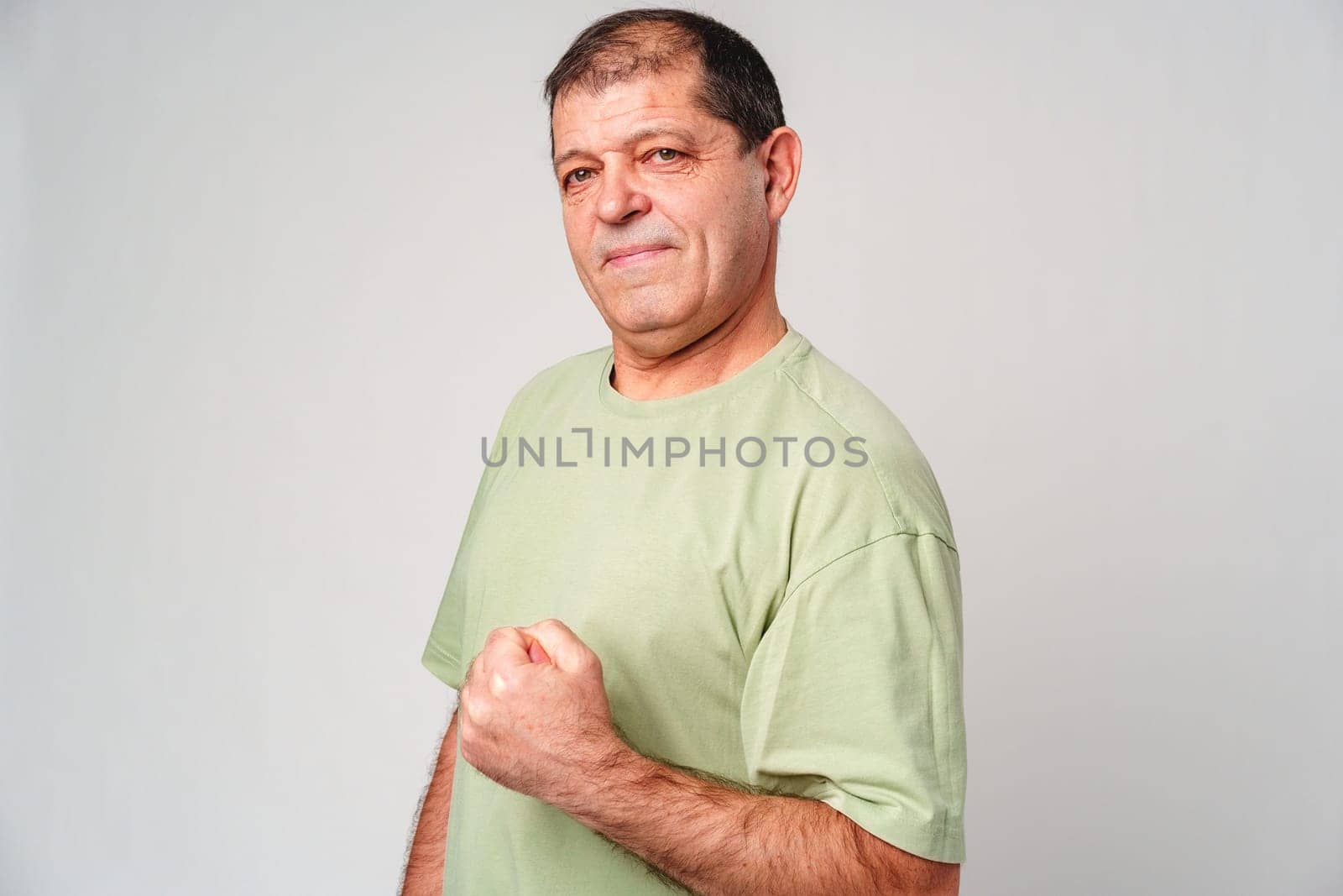 Confident older man posing with a clenched fist in a light green shirt against a neutral background close up