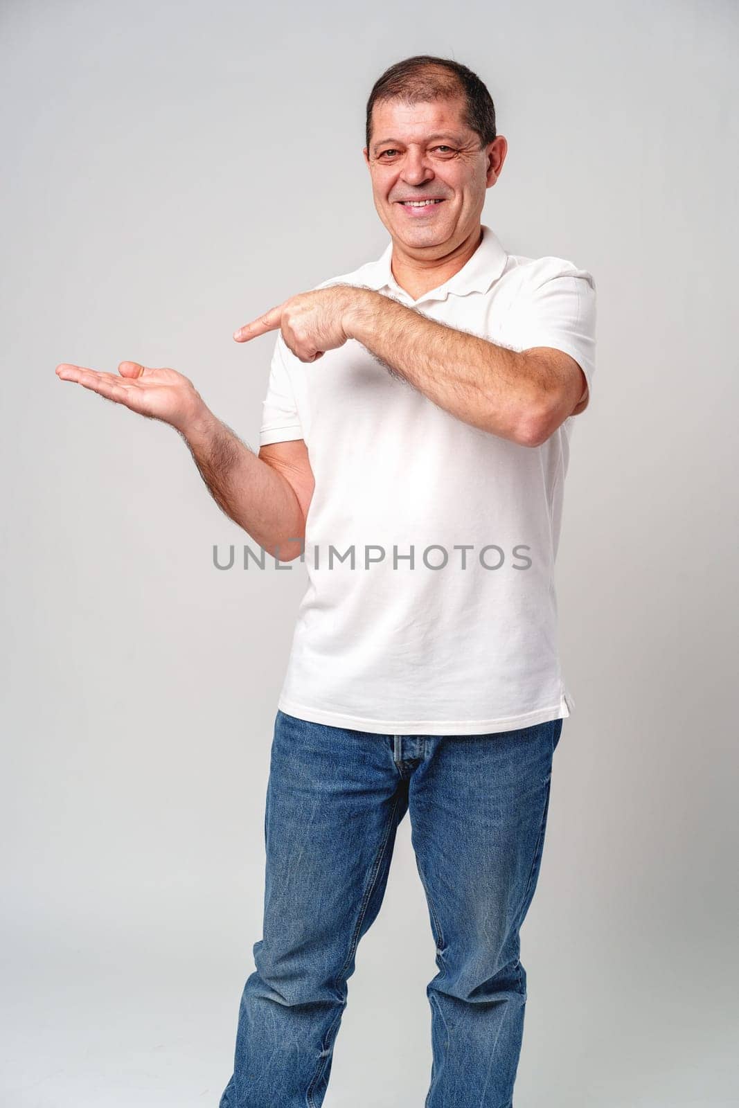 Man dressed in a white polo shirt and jeans happily pointing to the side against a plain background close up
